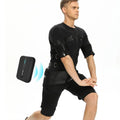 Man wearing a black electronic muscle stimulator suit device on his torso with a remote control nearby.